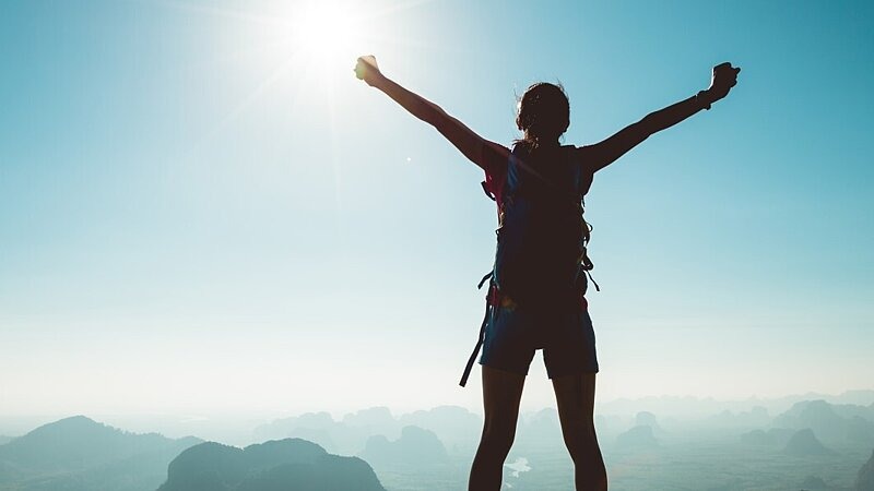 Frau mit Backpacker genießt die Aussicht auf einer Bergspitze und jubelt , stock.adobe.com / Colin
