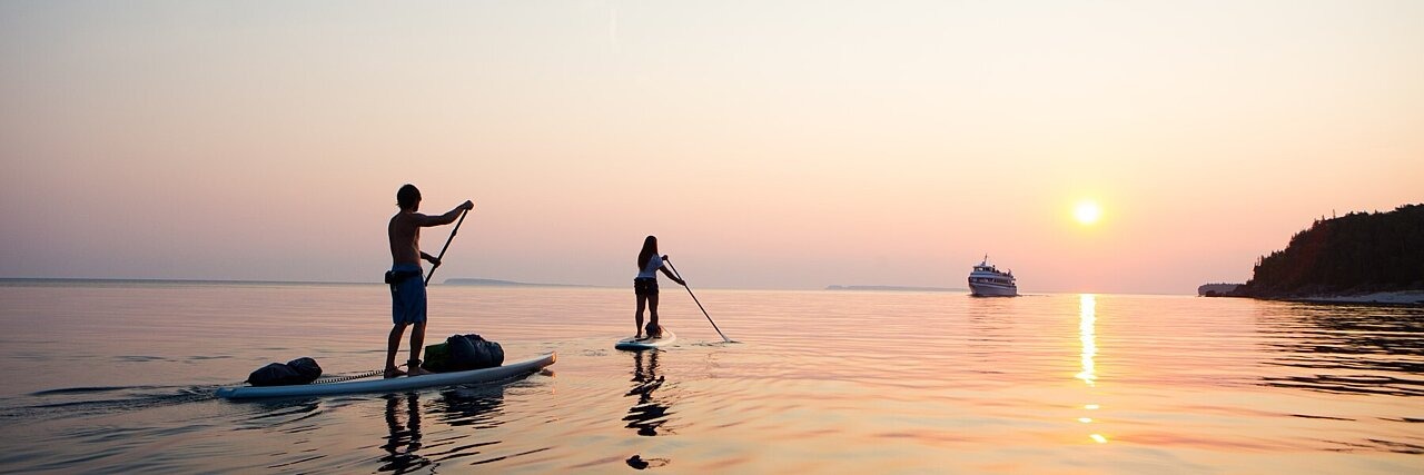 Zwei Personen beim Stand-up-Paddling bei Sonnenuntergang.