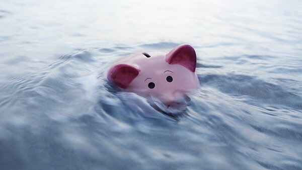 Ein pinkes Sparschwein sinkt im Wasser – Symbolbild für finanzielle Probleme als Folge einer Glücksspielsucht.
